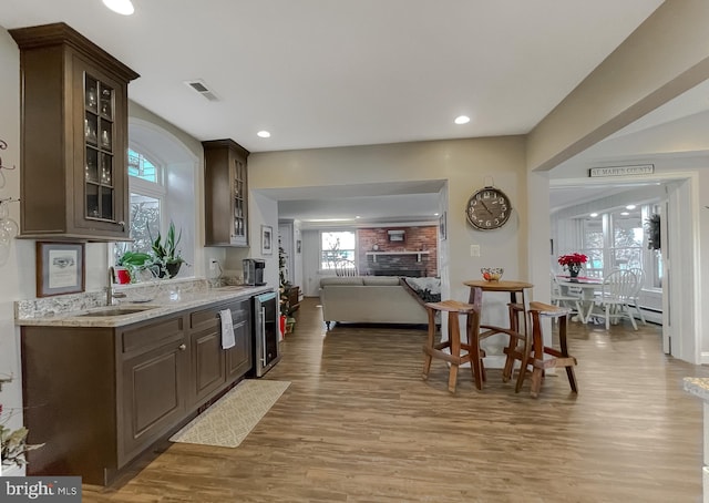 kitchen with light stone counters, dark brown cabinetry, beverage cooler, a fireplace, and light hardwood / wood-style floors