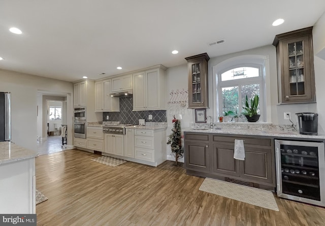 kitchen featuring light stone counters, stainless steel appliances, beverage cooler, sink, and light hardwood / wood-style flooring