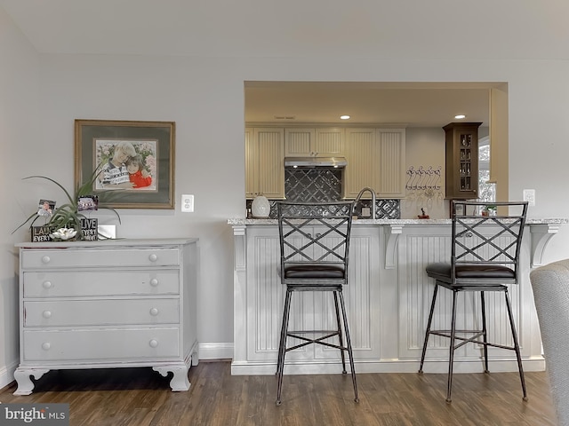 kitchen featuring a kitchen bar, dark hardwood / wood-style flooring, backsplash, light stone counters, and cream cabinetry