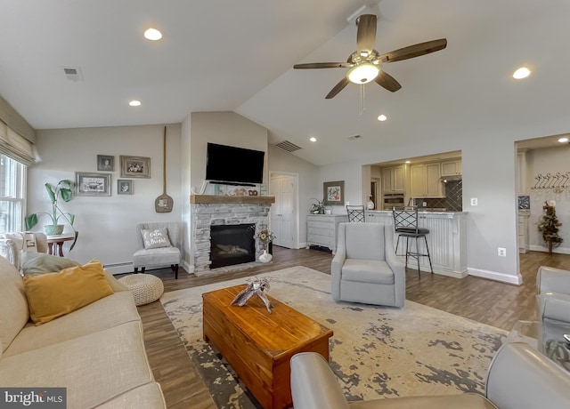 living room featuring hardwood / wood-style flooring, ceiling fan, a stone fireplace, and lofted ceiling