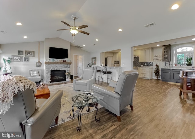 living room with ceiling fan, a stone fireplace, lofted ceiling, and light hardwood / wood-style flooring