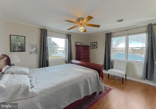 bedroom with ceiling fan, crown molding, a water view, and wood-type flooring