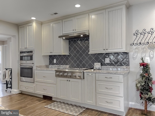 kitchen with decorative backsplash, appliances with stainless steel finishes, light wood-type flooring, and light stone counters