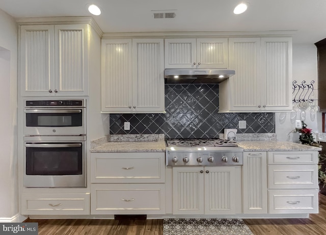 kitchen with dark hardwood / wood-style floors, light stone countertops, stainless steel appliances, and tasteful backsplash