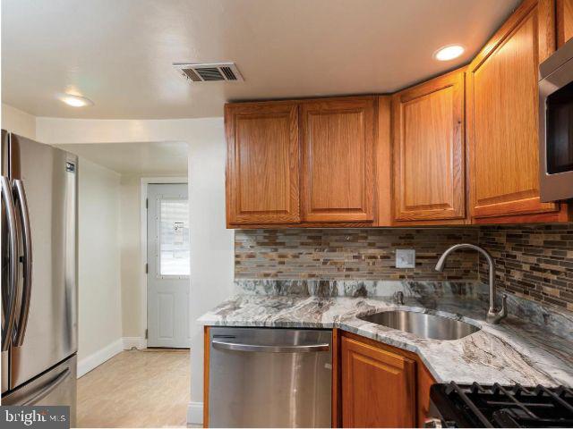 kitchen with decorative backsplash, appliances with stainless steel finishes, light stone counters, and sink