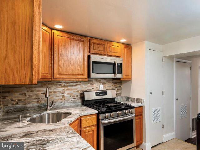 kitchen featuring light stone countertops, decorative backsplash, sink, and stainless steel appliances