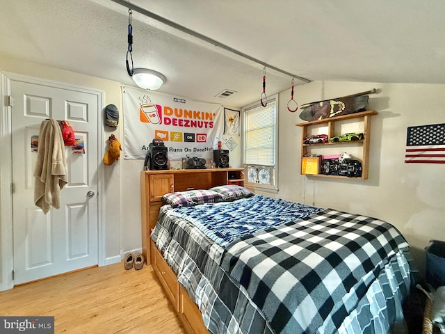 bedroom featuring a textured ceiling, light wood-type flooring, and lofted ceiling