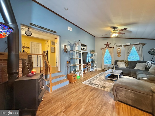 living room with a wood stove, ceiling fan, crown molding, hardwood / wood-style floors, and vaulted ceiling