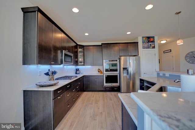 kitchen featuring stainless steel appliances, decorative light fixtures, dark brown cabinets, light hardwood / wood-style flooring, and sink