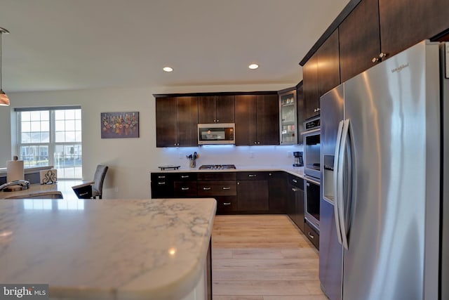 kitchen featuring appliances with stainless steel finishes, decorative light fixtures, sink, light wood-type flooring, and dark brown cabinets