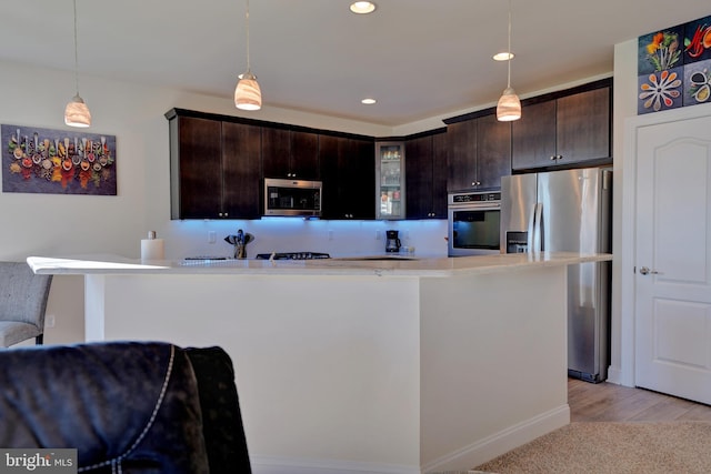 kitchen with dark brown cabinets, pendant lighting, stainless steel appliances, and light wood-type flooring