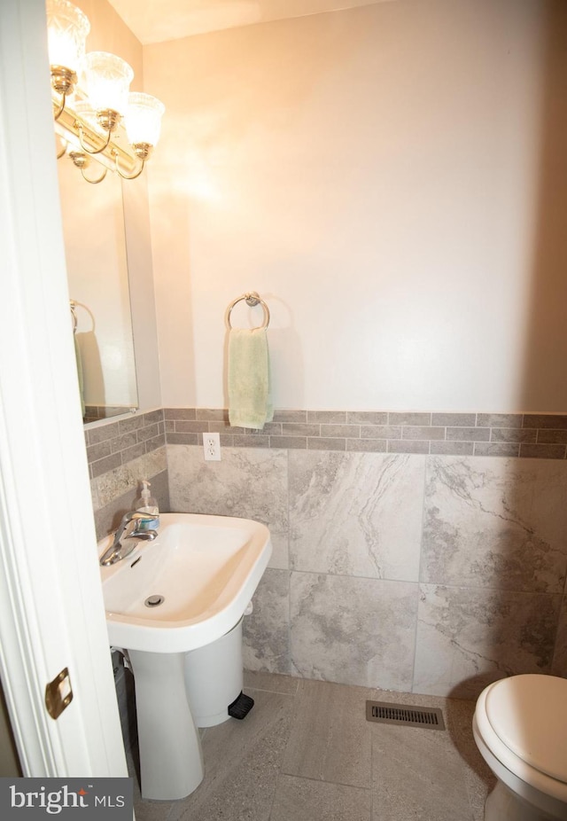 bathroom with toilet, tile patterned flooring, tile walls, and a notable chandelier