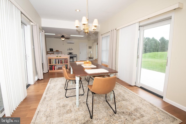 dining space featuring ceiling fan with notable chandelier, light wood-type flooring, and an AC wall unit