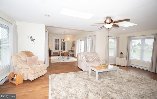 living room featuring ceiling fan with notable chandelier, light hardwood / wood-style floors, a skylight, and a healthy amount of sunlight