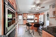 kitchen with a kitchen bar, stainless steel oven, ceiling fan, white fridge, and light tile patterned flooring