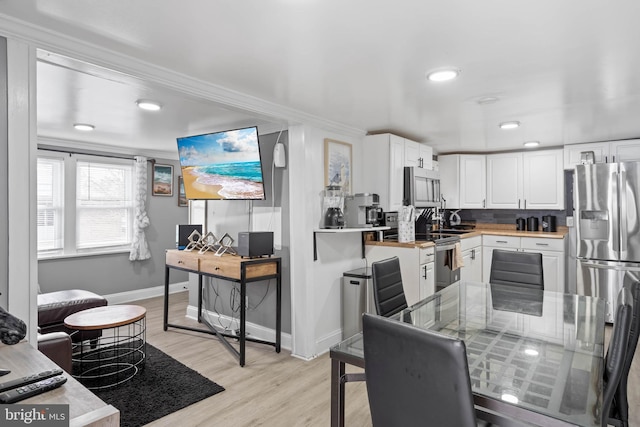 kitchen featuring stainless steel appliances, crown molding, light hardwood / wood-style flooring, white cabinets, and butcher block counters