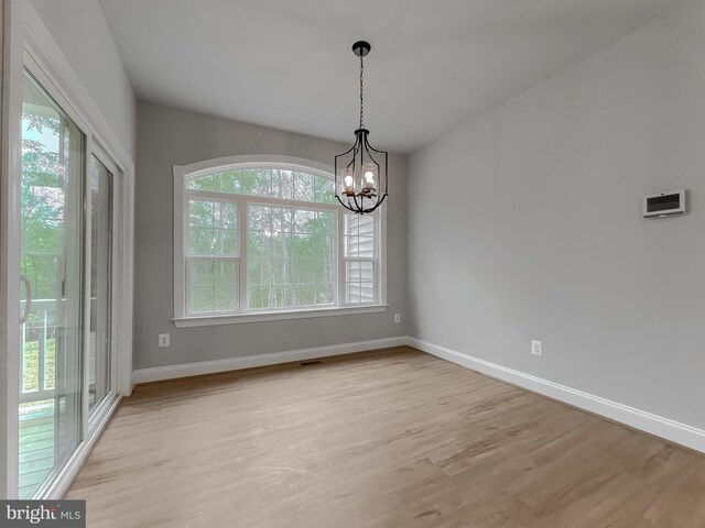 unfurnished dining area with baseboards, a notable chandelier, light wood-style flooring, and plenty of natural light