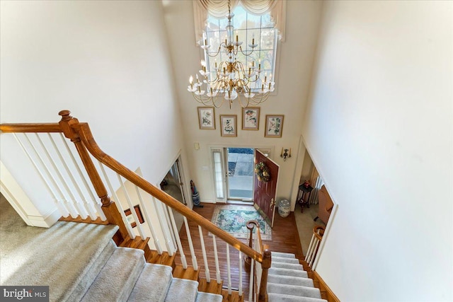 stairway featuring a towering ceiling, wood-type flooring, and a notable chandelier