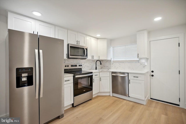 kitchen featuring appliances with stainless steel finishes, light wood-type flooring, white cabinetry, and backsplash