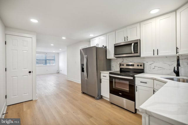 kitchen with decorative backsplash, appliances with stainless steel finishes, light stone counters, light hardwood / wood-style floors, and white cabinetry