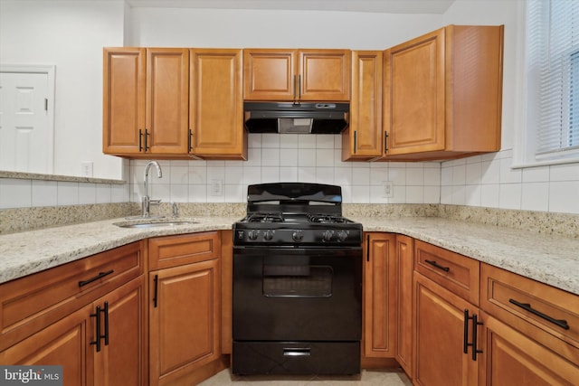 kitchen featuring black gas range, backsplash, light stone counters, and sink