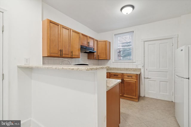 kitchen featuring light stone countertops, kitchen peninsula, white fridge, decorative backsplash, and light tile patterned floors