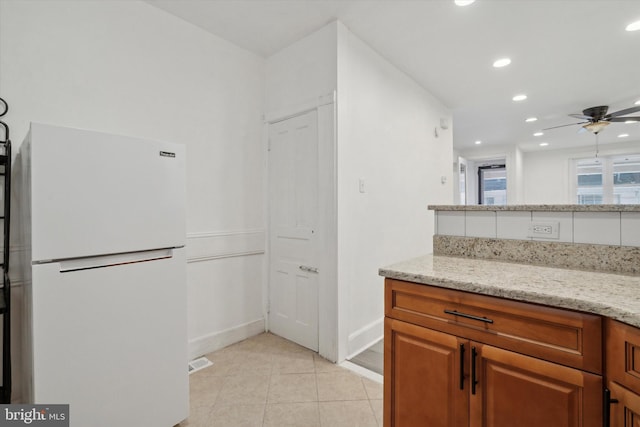 kitchen featuring light stone countertops, white refrigerator, ceiling fan, and light tile patterned flooring