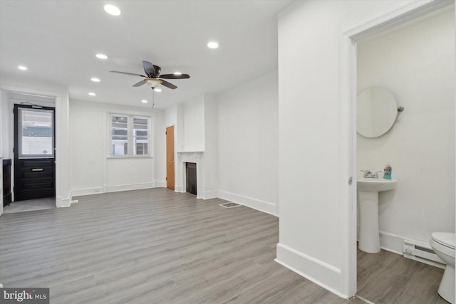 unfurnished living room featuring ceiling fan, light hardwood / wood-style floors, and a baseboard heating unit