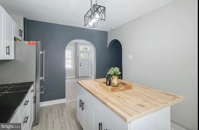 kitchen featuring stainless steel fridge, a kitchen island, pendant lighting, light hardwood / wood-style floors, and white cabinetry