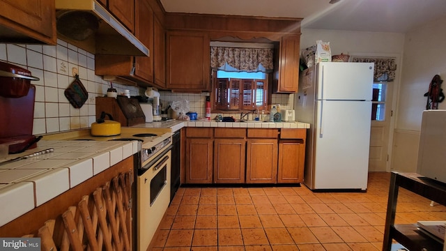 kitchen with backsplash, white refrigerator, sink, tile counters, and light tile patterned flooring