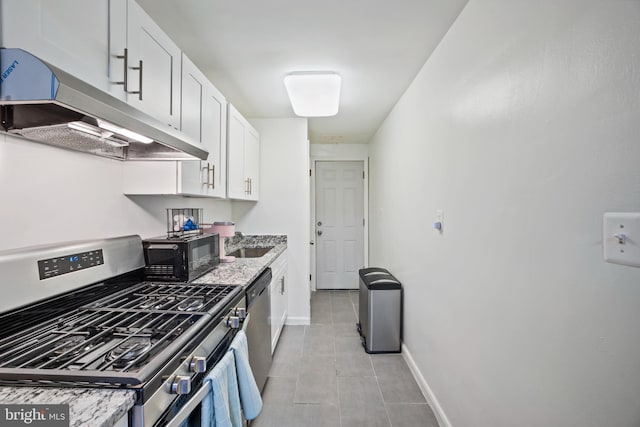 kitchen with sink, light tile patterned floors, appliances with stainless steel finishes, light stone counters, and white cabinetry