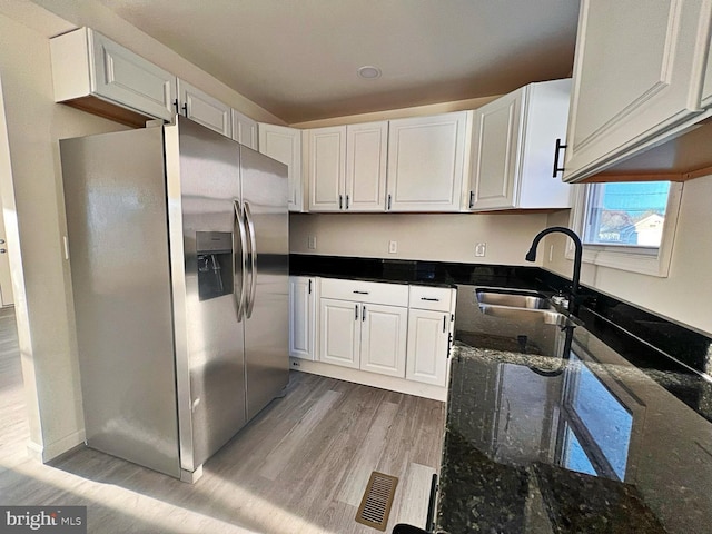 kitchen featuring light hardwood / wood-style floors, white cabinetry, stainless steel fridge with ice dispenser, and dark stone counters