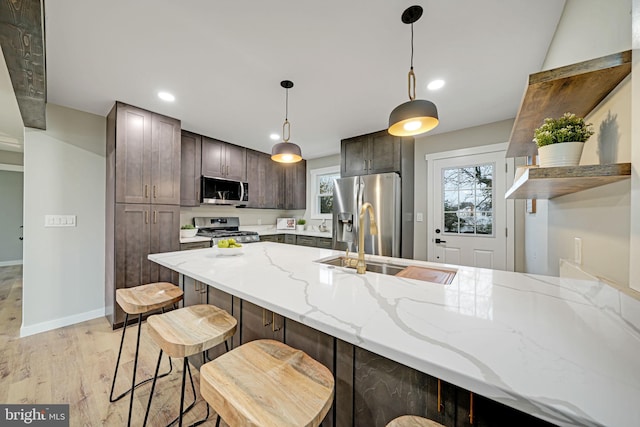 kitchen featuring appliances with stainless steel finishes, light stone counters, dark brown cabinetry, pendant lighting, and light hardwood / wood-style floors