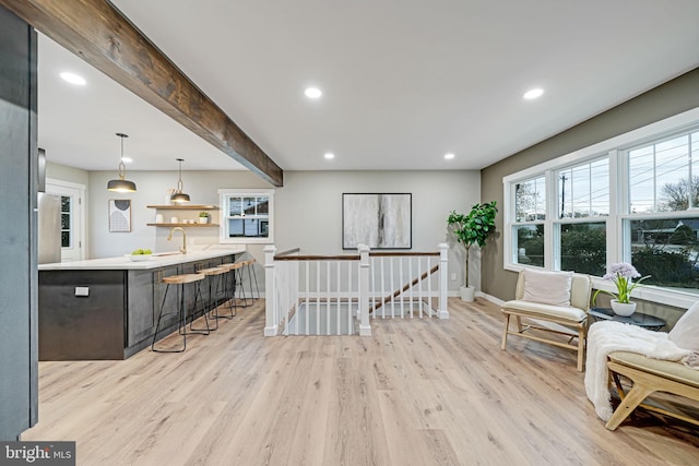 living area with beam ceiling, sink, and light hardwood / wood-style flooring