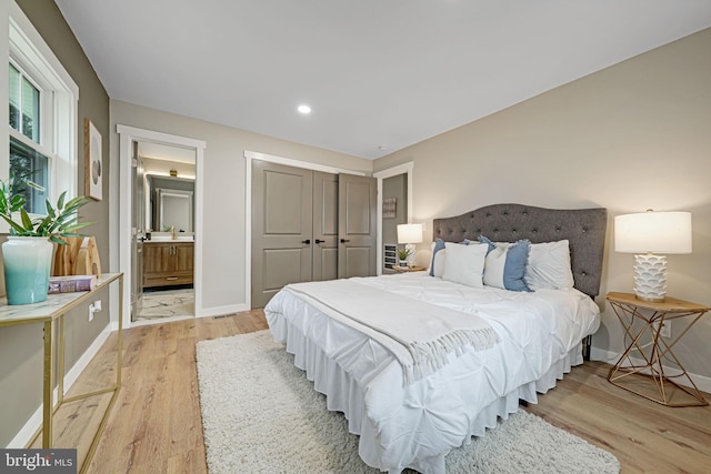 bedroom featuring connected bathroom, a closet, light hardwood / wood-style flooring, and sink