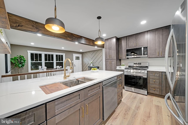 kitchen with pendant lighting, sink, light wood-type flooring, appliances with stainless steel finishes, and light stone counters