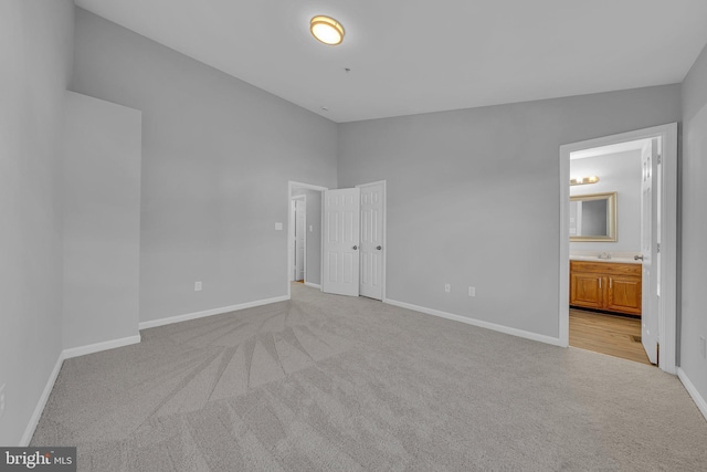 unfurnished bedroom with light carpet, ensuite bathroom, vaulted ceiling, and sink