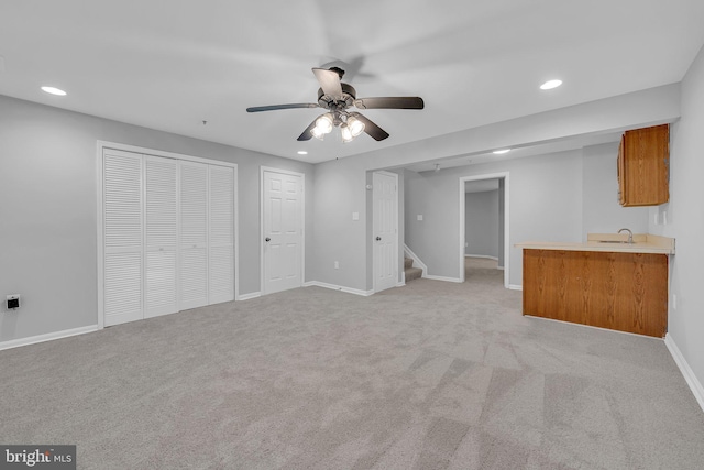 unfurnished living room featuring light carpet, sink, and ceiling fan