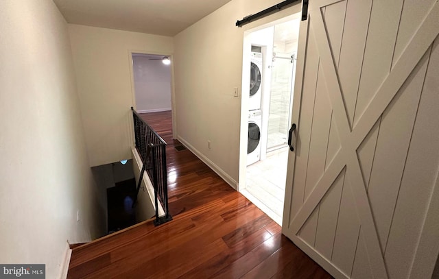 washroom with a barn door, stacked washing maching and dryer, and dark hardwood / wood-style floors