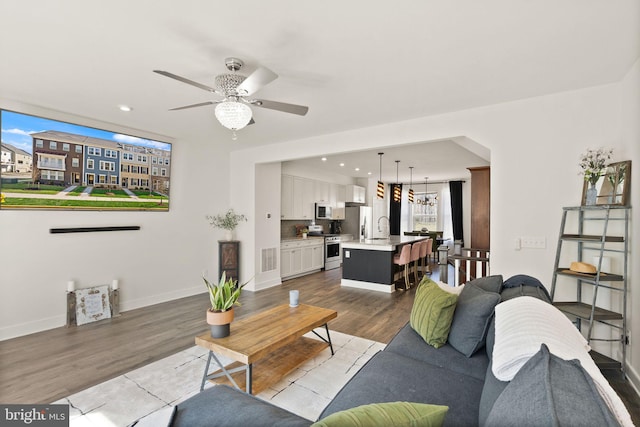 living area with recessed lighting, visible vents, wood finished floors, baseboards, and ceiling fan with notable chandelier