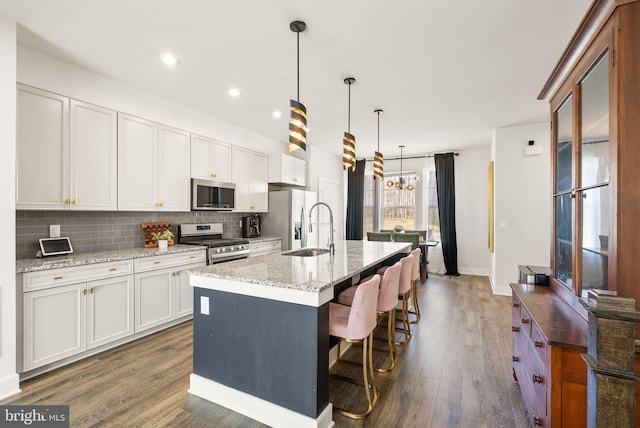 kitchen featuring tasteful backsplash, a center island with sink, dark wood-type flooring, stainless steel appliances, and a sink