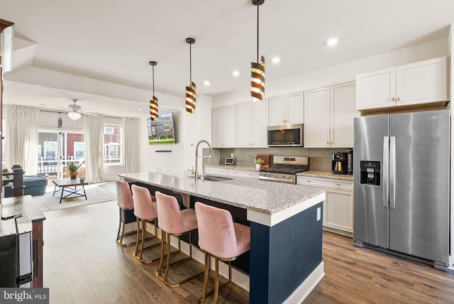 kitchen with a kitchen island with sink, a sink, appliances with stainless steel finishes, dark wood-style floors, and tasteful backsplash