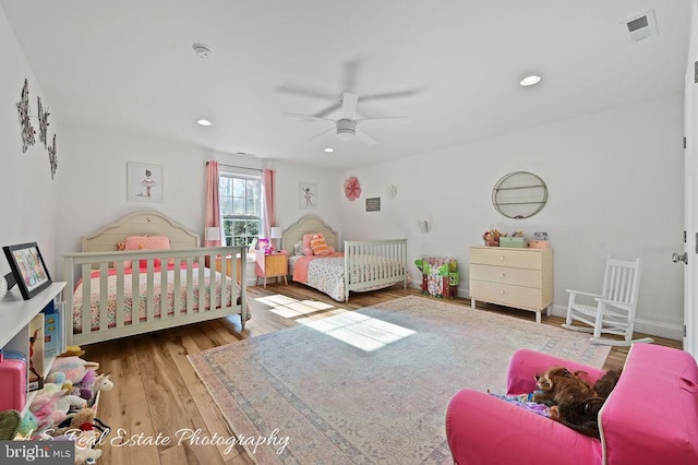 bedroom featuring ceiling fan, a crib, and hardwood / wood-style flooring