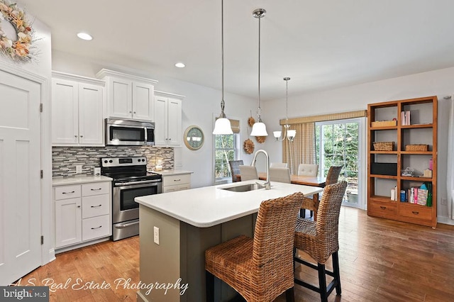 kitchen featuring sink, an island with sink, decorative light fixtures, white cabinetry, and stainless steel appliances