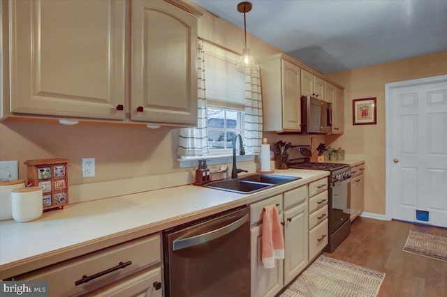 kitchen with sink, stainless steel appliances, decorative light fixtures, light brown cabinetry, and light wood-type flooring