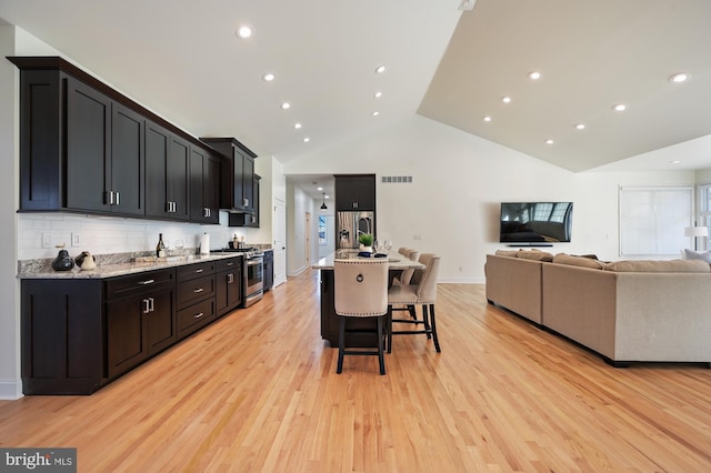 kitchen with a kitchen breakfast bar, a spacious island, light hardwood / wood-style flooring, decorative backsplash, and stainless steel appliances