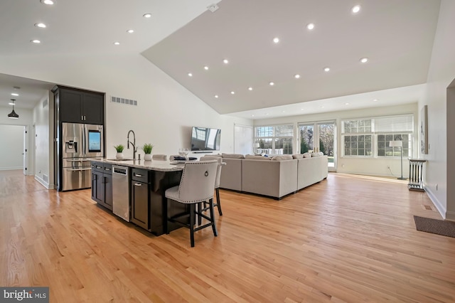 kitchen with light stone countertops, light wood-type flooring, a breakfast bar, stainless steel appliances, and a center island with sink