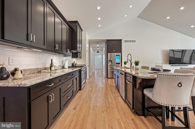 kitchen featuring a kitchen bar, backsplash, stainless steel appliances, vaulted ceiling, and a center island with sink