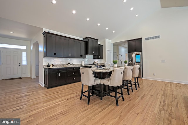 kitchen featuring a kitchen bar, stainless steel refrigerator with ice dispenser, light wood-type flooring, tasteful backsplash, and a kitchen island with sink