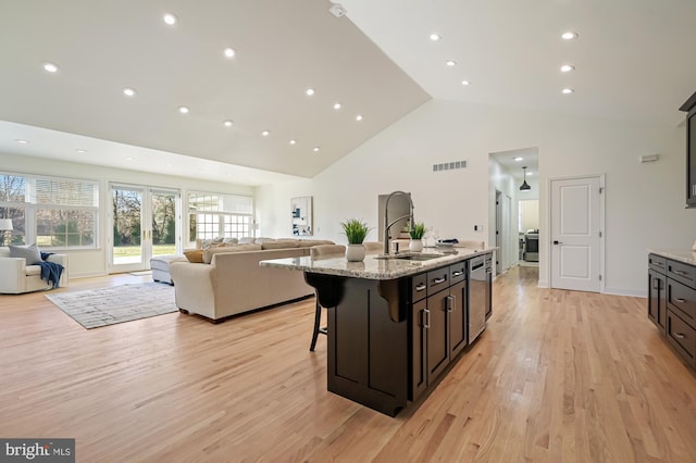 kitchen featuring a kitchen bar, light stone counters, a kitchen island with sink, sink, and light hardwood / wood-style floors